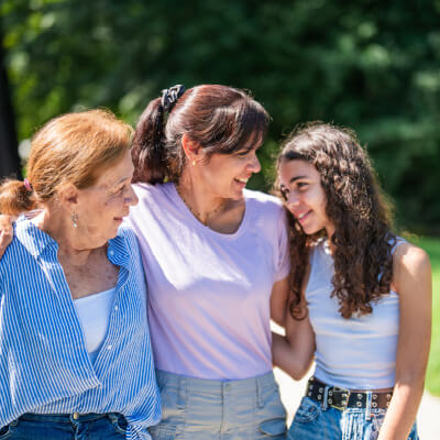 Three women standing together outdoors with greenery in the background.