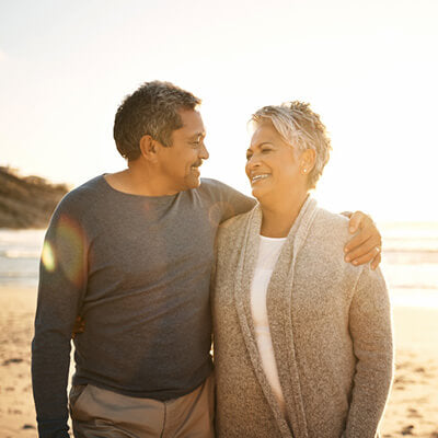 Man and woman standing close together on a beach, smiling at each other.
