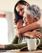 Woman hugging an older woman at a table with a mug and book.