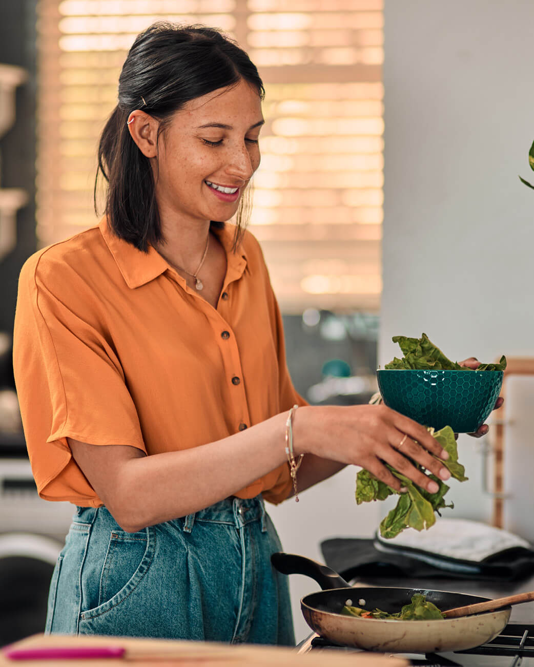 Woman in an orange shirt preparing food in a kitchen.