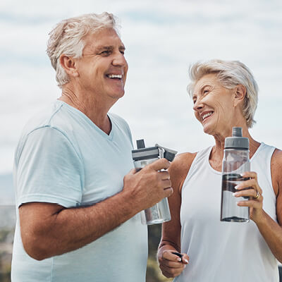 Two elderly people holding water bottles outdoors.