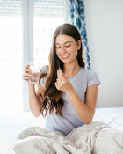 Woman in bed holding a glass of water and a supplement pill.