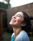 Woman laughing outdoors with a blurred background.