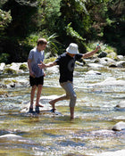 Two people crossing a river with trees and rocks in the background.