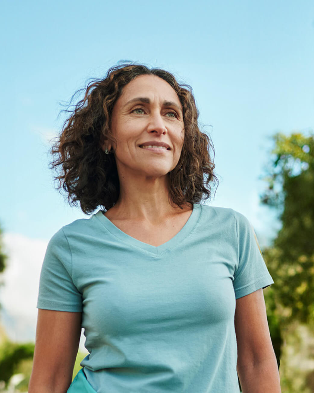 Woman wearing a light blue t-shirt outdoors with a clear sky background.