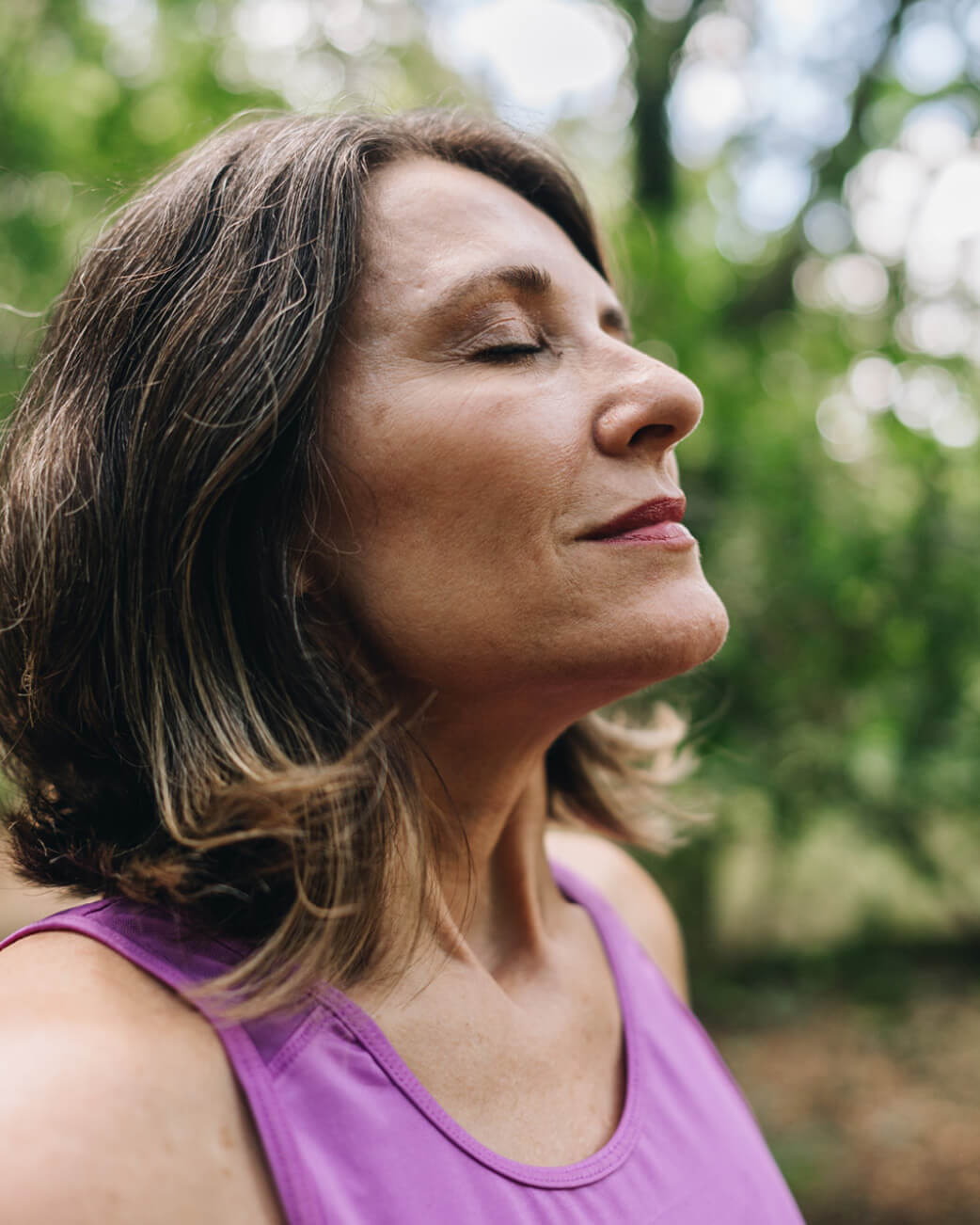 Woman in a purple tank top with a blurred green background.