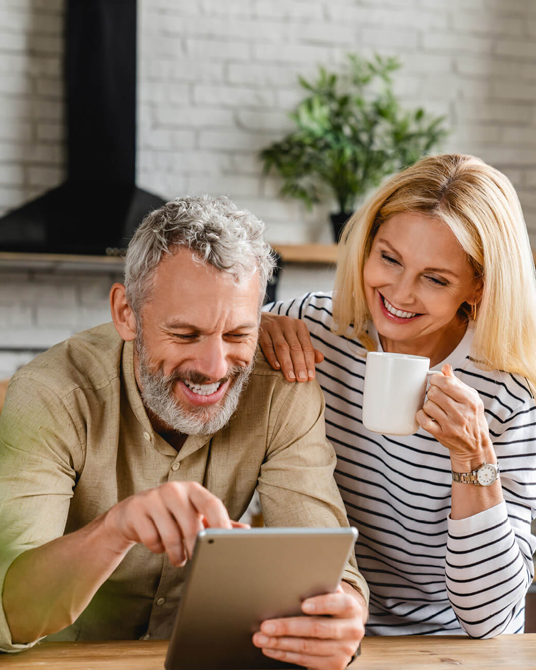 Woman and man smiling over a tablet in a kitchen.