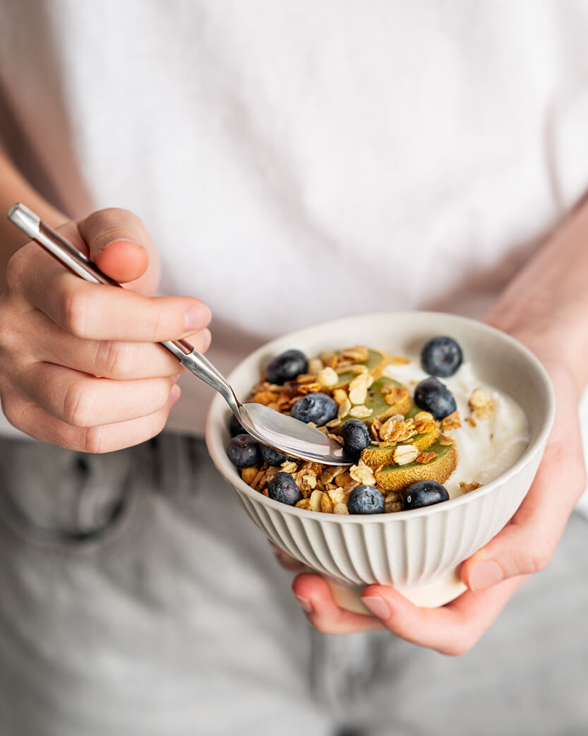 Person holding a bowl of cereal with blueberries and a spoon