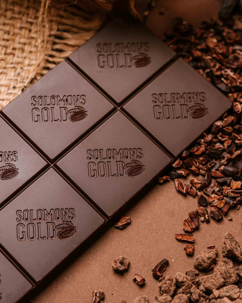 Dark chocolate bar with 'Solomon's Gold' branding on a textured surface with cocoa beans.