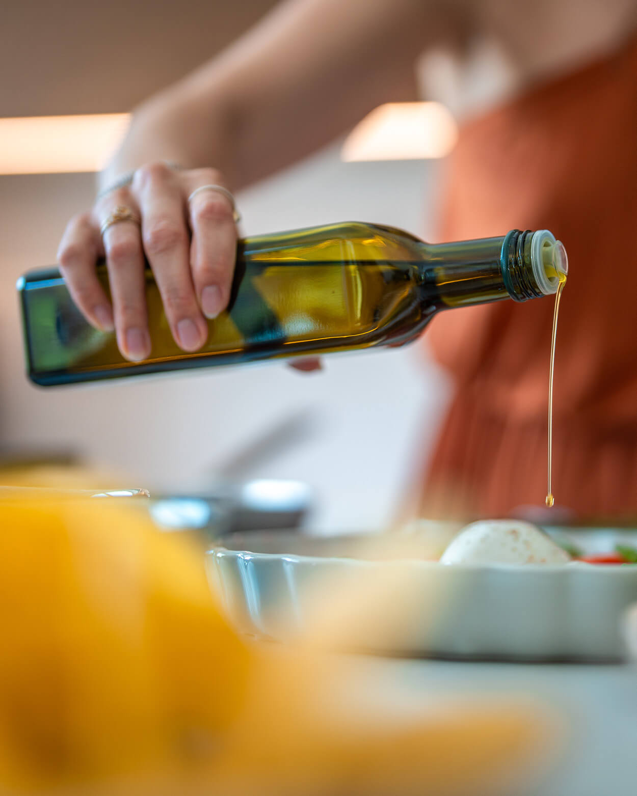 Person pouring olive oil from a bottle into a dish on a kitchen counter.