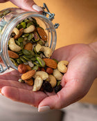 Hand holding a jar of mixed nuts and seeds with a blurred background.