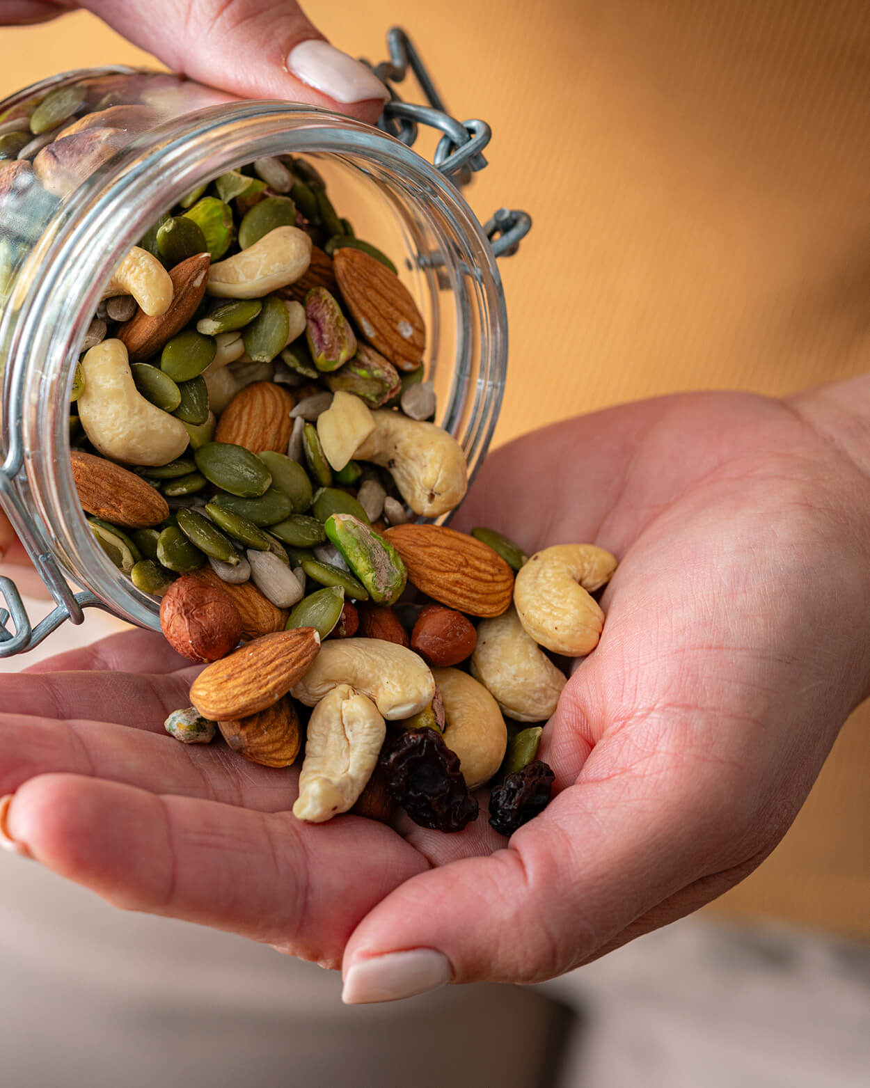 Hand holding a jar of mixed nuts and seeds with a blurred background.