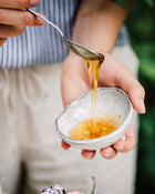 Honey being drizzled from a spoon into a small bowl held by a person.