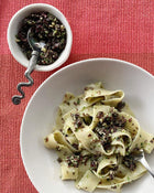 Pasta dish with a side of dark green seaweed sauce on a red textured surface