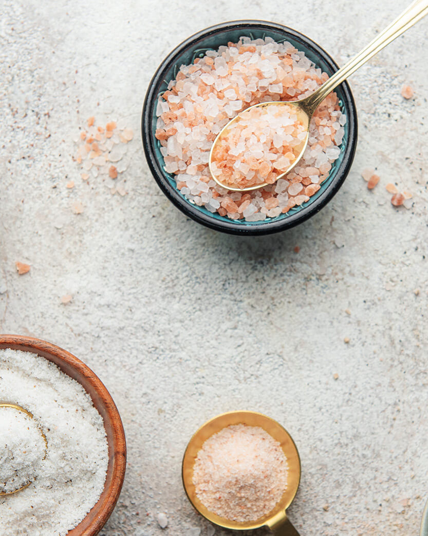 Bowl of pink himalayan salt with a gold spoon on a light stone surface.