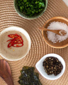 Assorted ingredients including red chili peppers, seaweed, and salt on a woven mat.