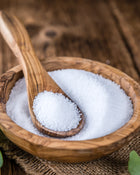 Wooden spoon in a bowl of white stevia granules on a wooden surface