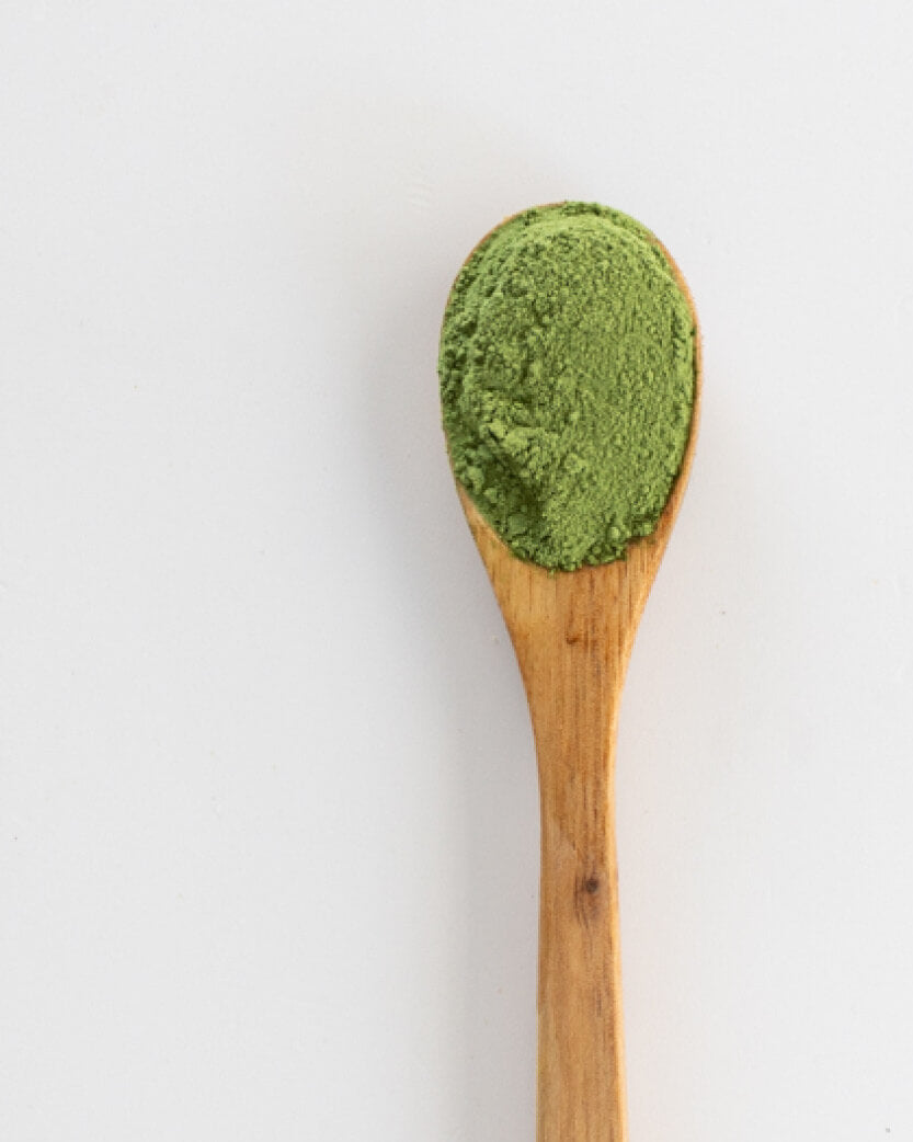 Wooden spoon filled with green powder on a white background