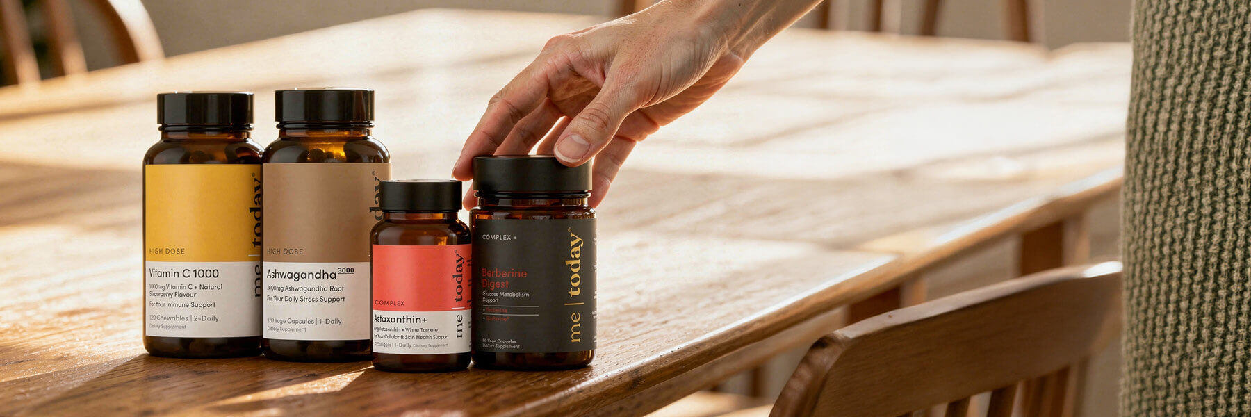 Hand reaching for Me Today supplement bottles on a wooden table.