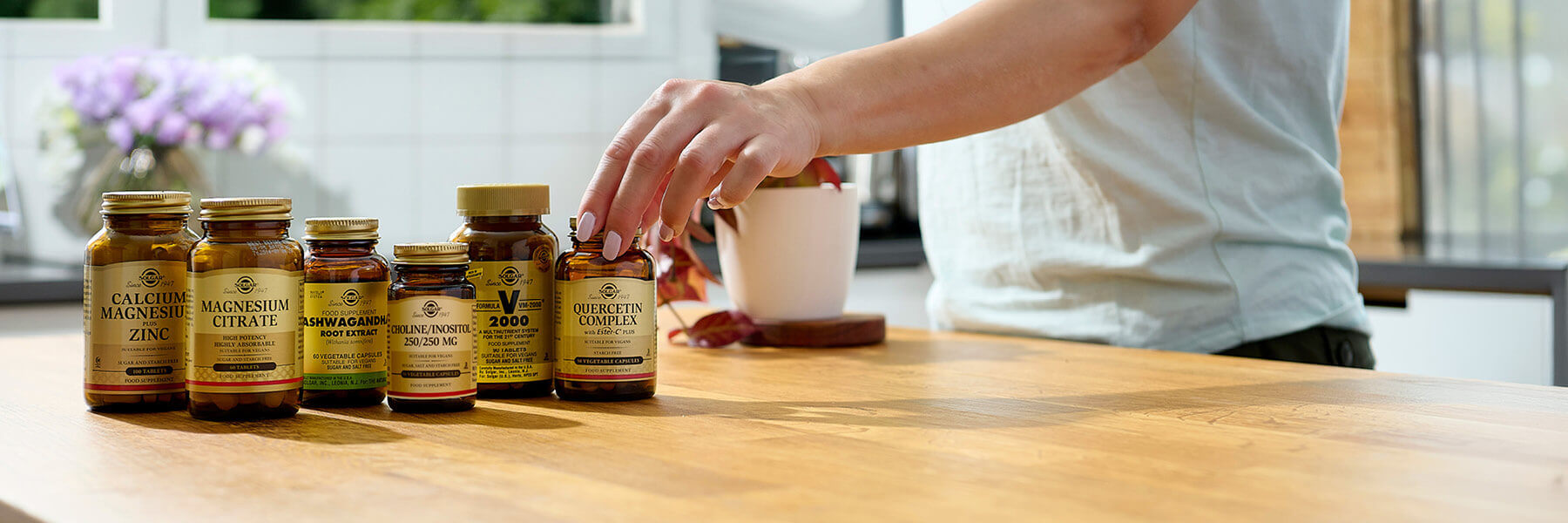 Hand picking Solgar supplement bottles on a wooden counter.