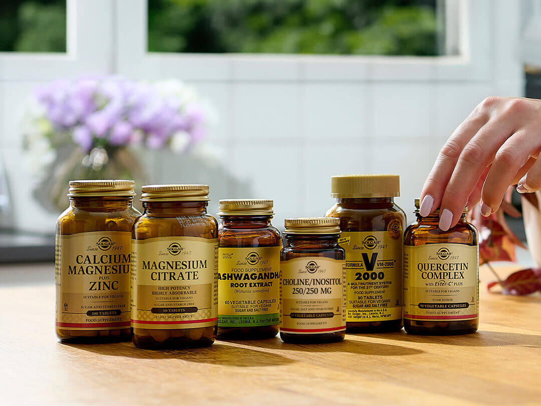 Hand picking Solgar supplement bottles on a wooden counter.