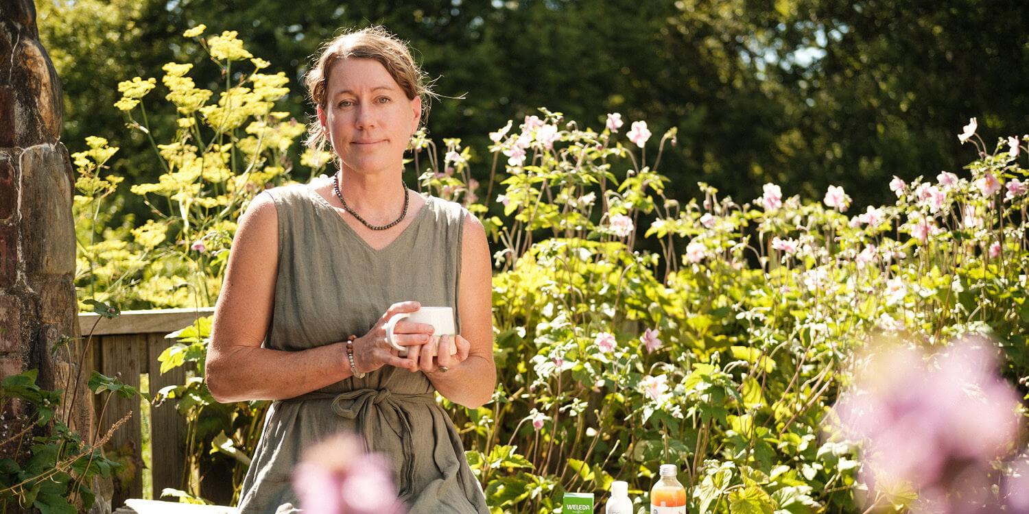 Woman holding a cup in a garden with flowers and plants around.