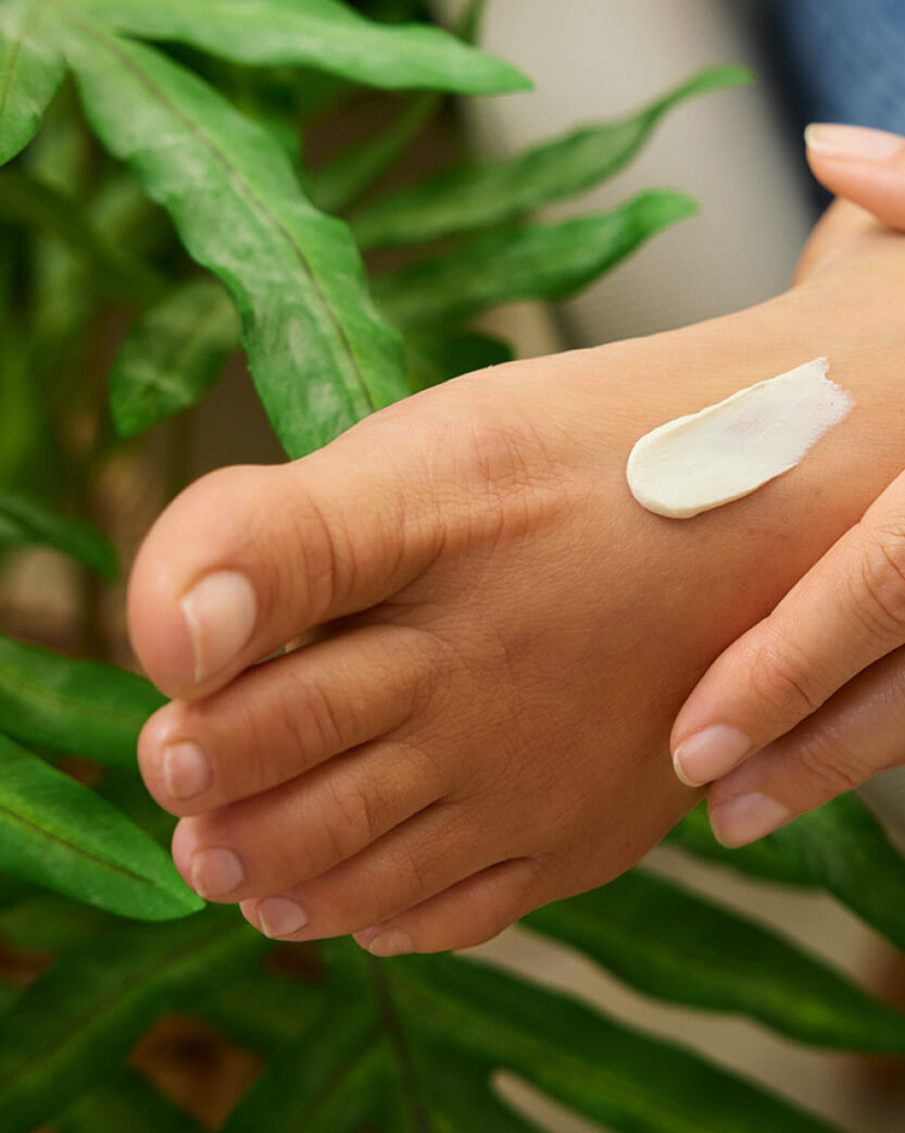 Hand applying cream with a green leafy background.