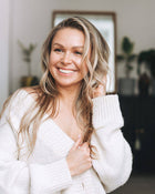 Woman wearing a white sweater indoors with a blurred background.
