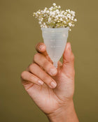 Hand holding a menstrual cup filled with baby's breath against a solid background.