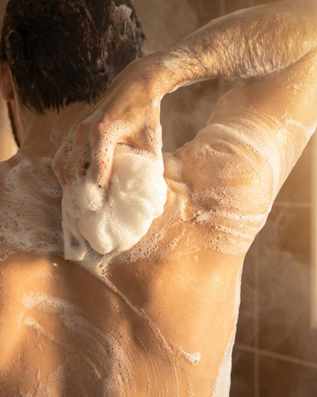 Man in the shower washing his back with a loofah.