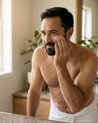 Man in a towel applying moisturiser to his face.