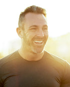 Man wearing a grey shirt smiling in a bright setting.