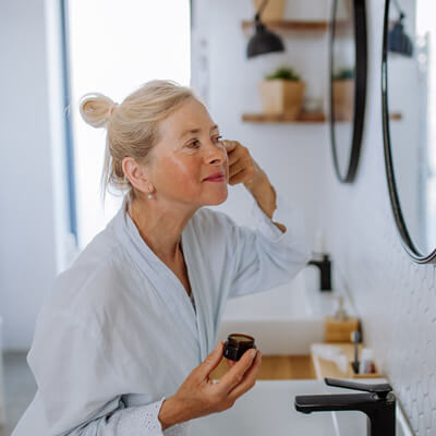 Woman applying cream to her face in a bathroom.