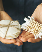 Hands holding a bundle of cotton swabs against a dark background.
