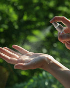 Person applying a spray to their hand with a blurred green background.
