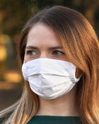Woman wearing a white face mask with a blurred natural background.