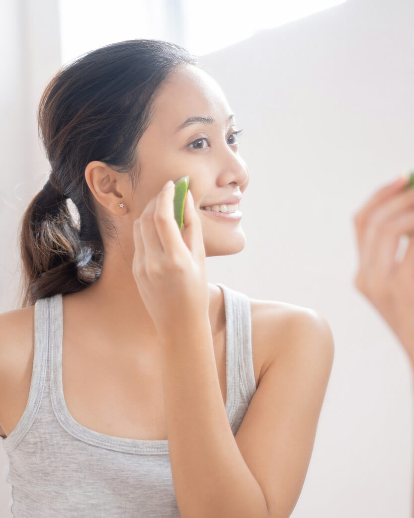 Woman applying a green facial mask to her face in a bright room.