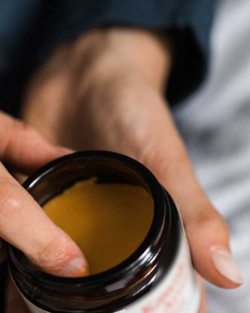 Hand holding a jar of yellow cream or paste.