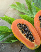 Halved papaya with seeds on a wooden surface with green leaves.