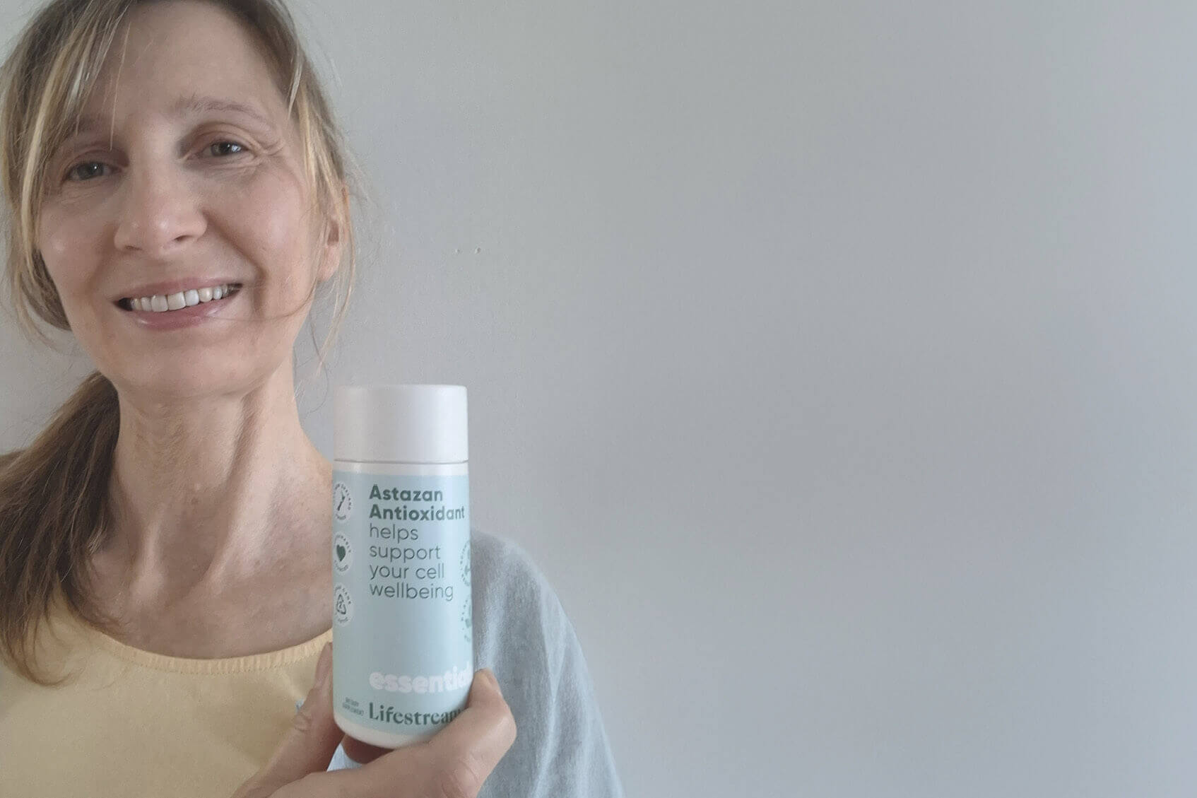 Woman holding a Astazan antioxidant product with a plain background