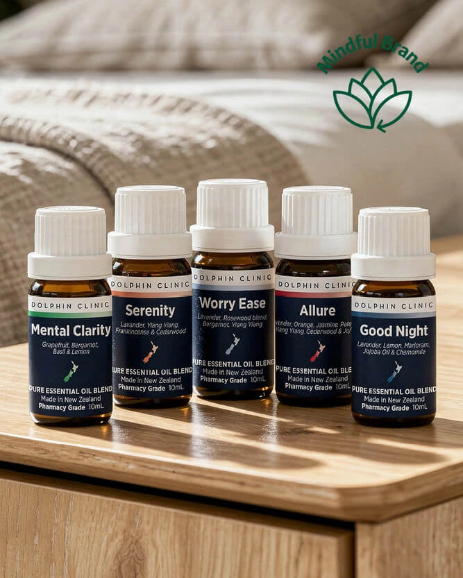 Five Dolphin Clinic essential oil bottles arranged on a wooden bedside table, with a soft neutral background and a green 'Mindful Brand' logo in the upper right.