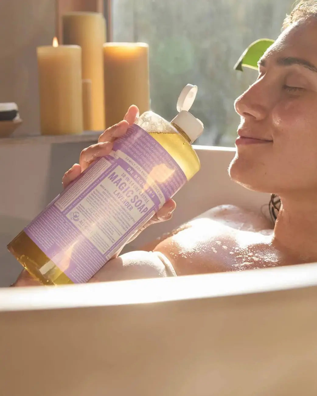 Person in a bath smelling Dr BRonners lavender magic soap.