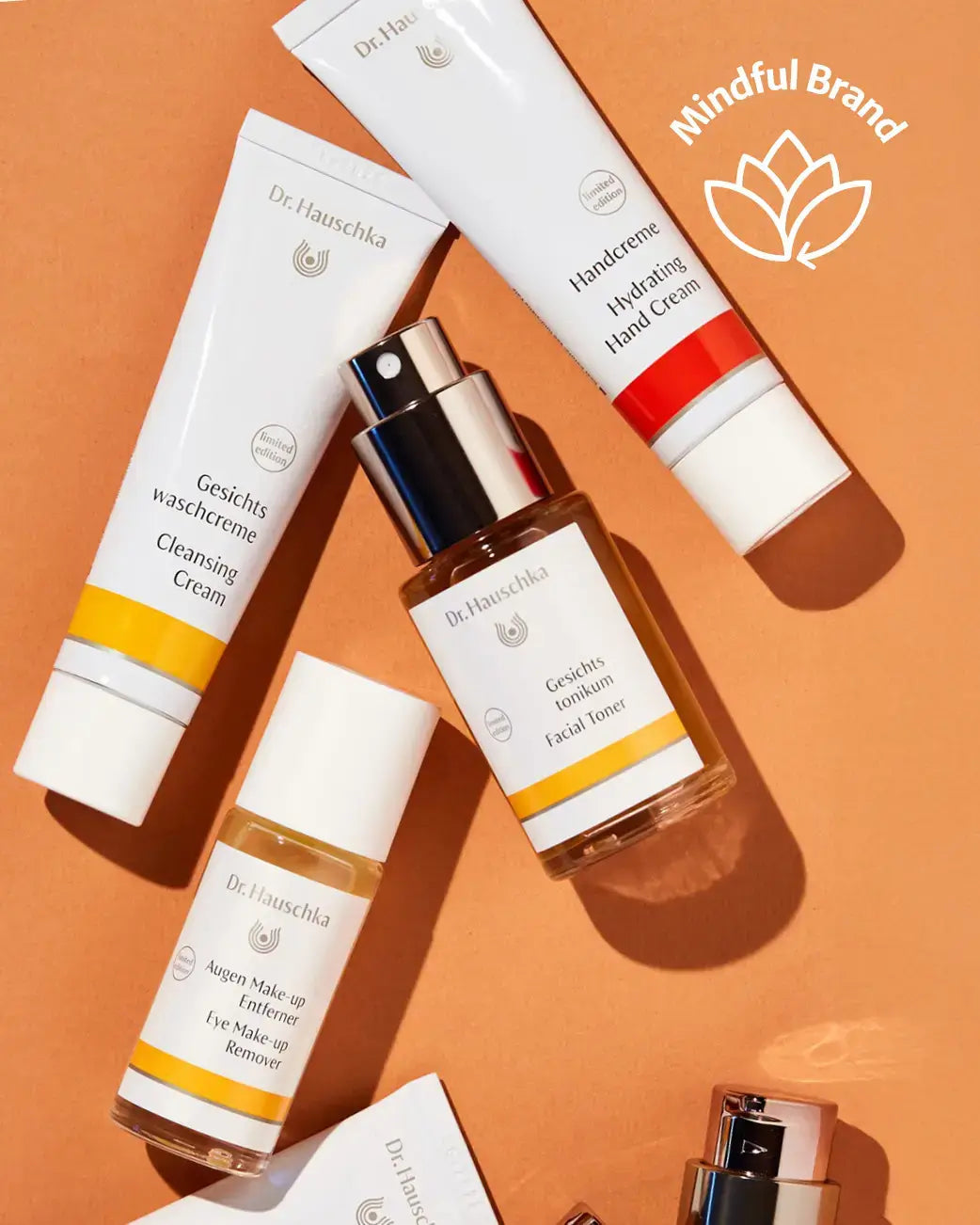 Cosmetic products with 'Dr. Hauschka' branding on an orange background, featuring the 'Mindful Brand' logo.