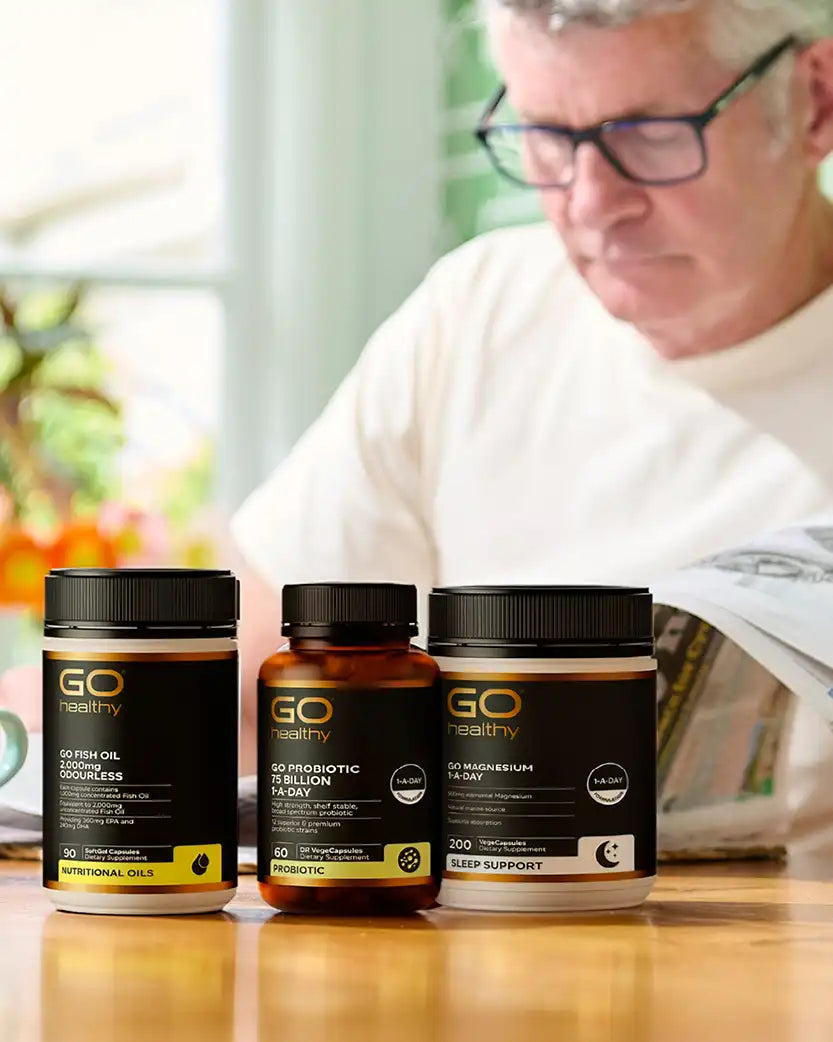 Three 'GO Healthy' supplement bottles on a table with a blurred background of a person reading a newspaper.