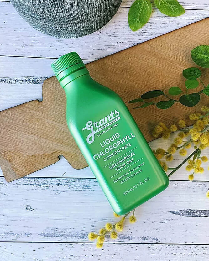 Green bottle of Liquid Chlorophyll Concentrate on a wooden surface with plants and flowers.