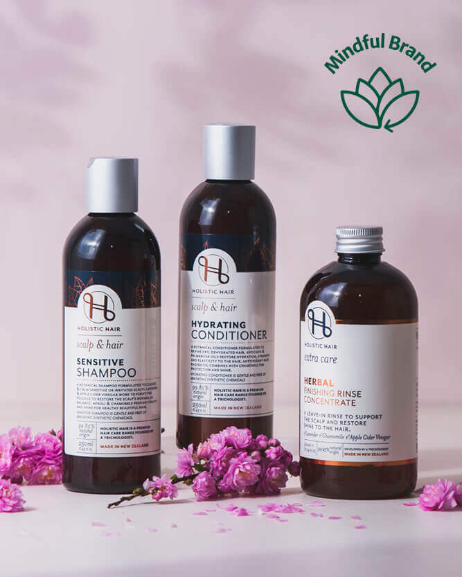 Three bottles of 'Holistic Hair' products with pink flowers on a light background, featuring the Mindful Brand logo.