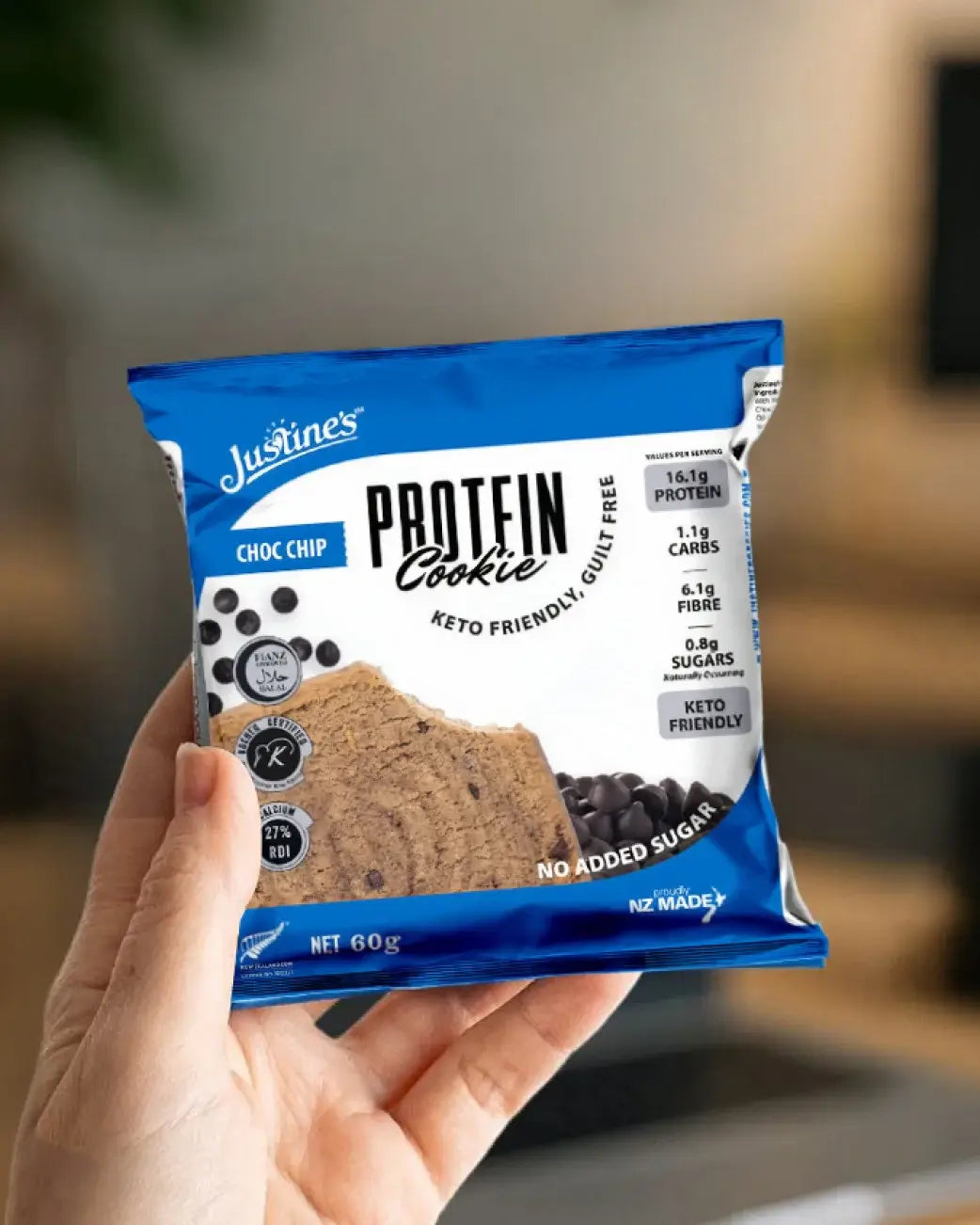 Hand holding a Justine's Protein Cookie package with a blurred background.