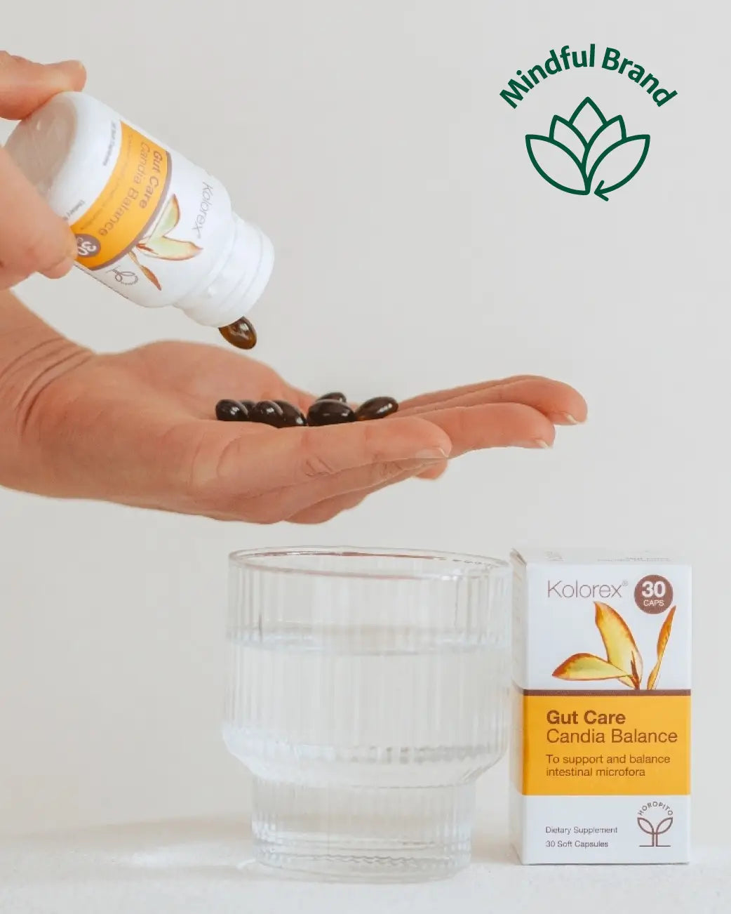 Person tipping out Kolorex Gut Care softgels onto hand with a glass of water and box packaging on a white surface.
