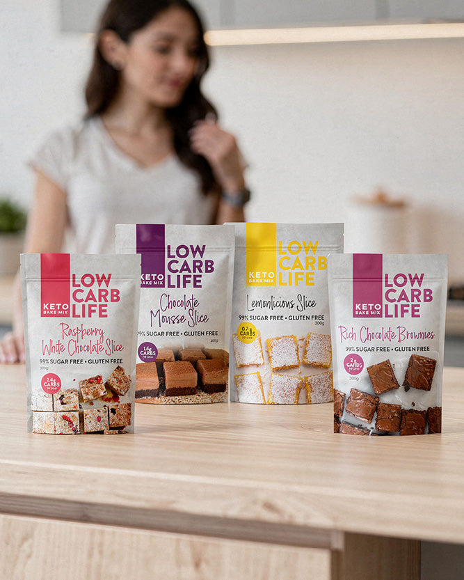 Four packages of 'Low Carb Life' products on a table with a blurred person in the background.