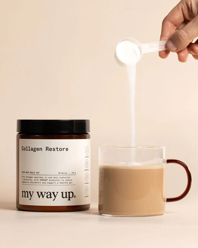 Person adding a scoop of collagen powder to a mug of coffee with 'my way up' product visible.